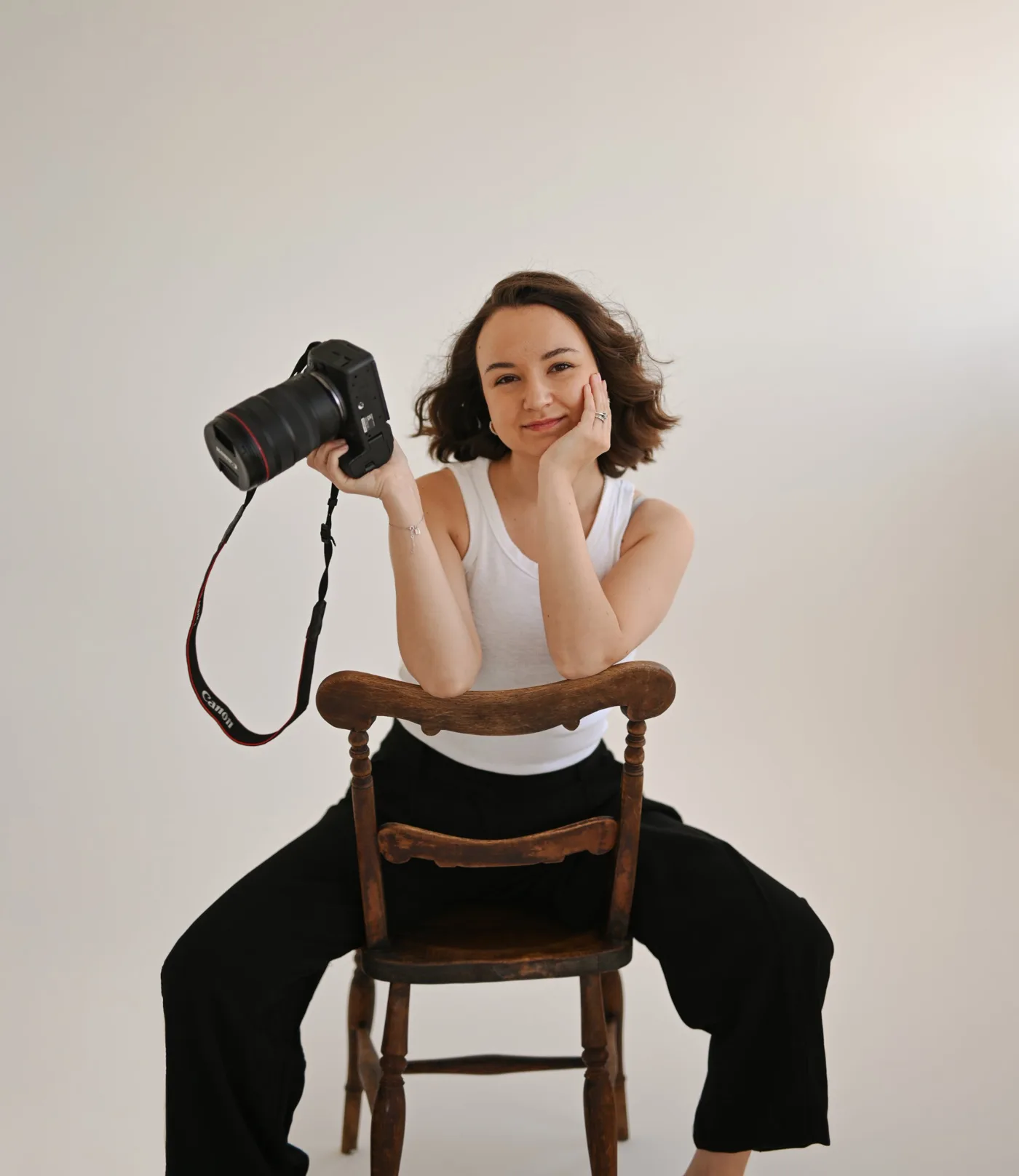 Lena Barber sitting on a wooden chair, holding her camera and smiling